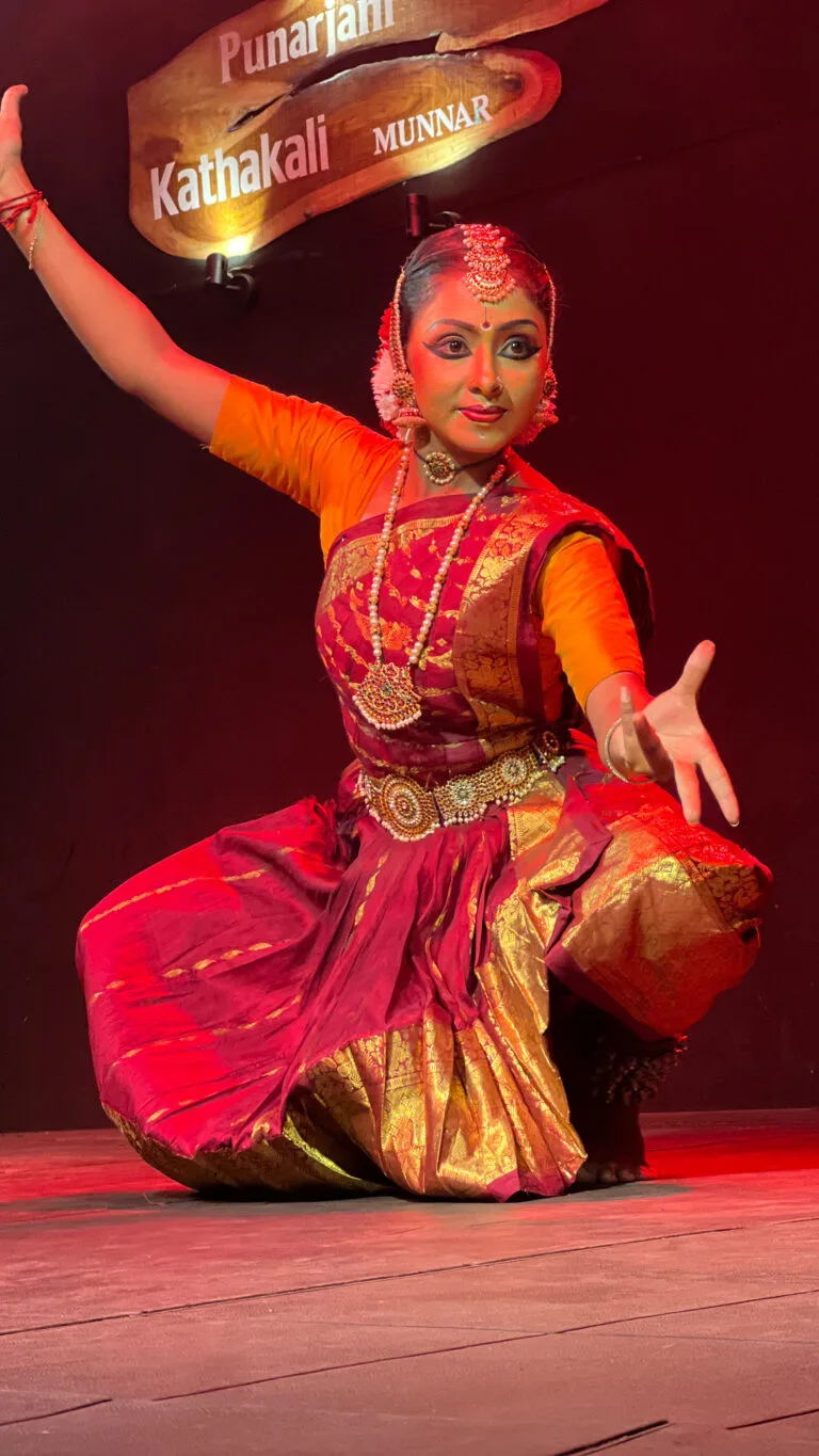 A classical dancer in a red and gold costume holds an expressive pose on stage