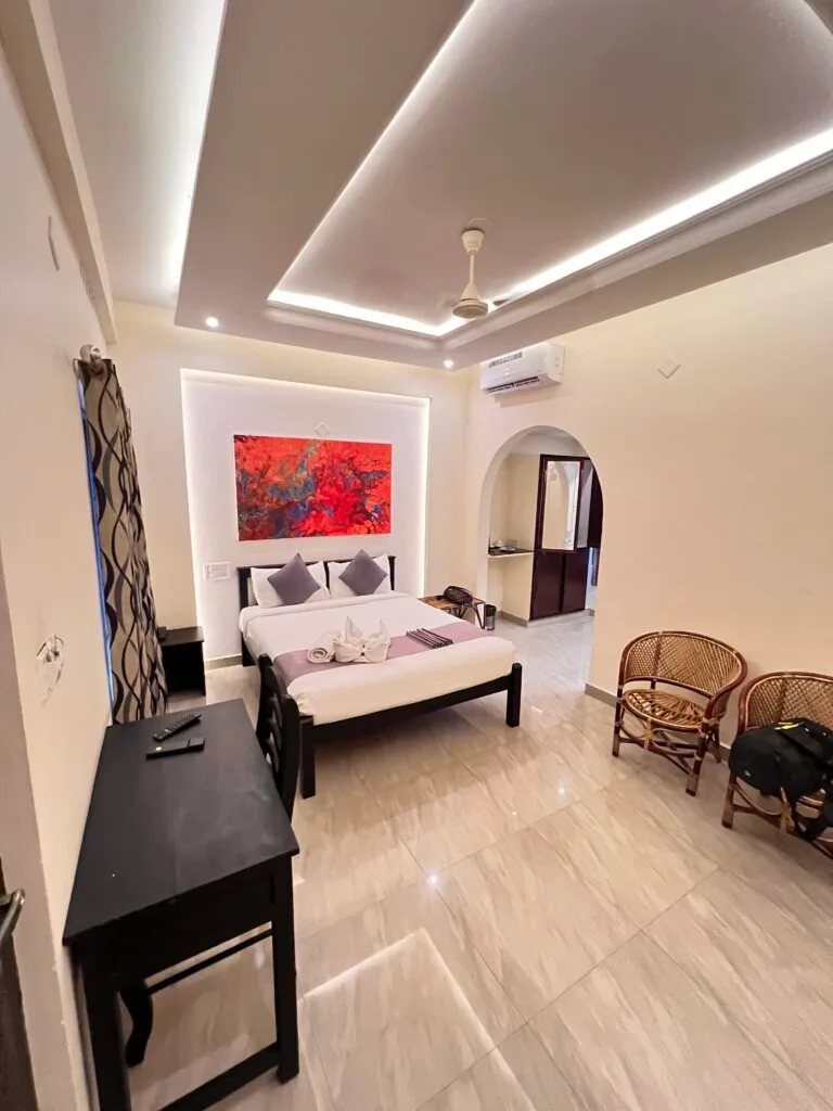 A bright guest room with a double bed, wooden chairs and a painting on the wall