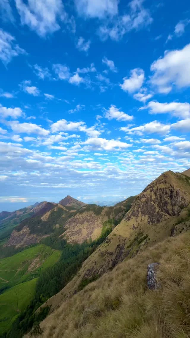 A rugged green ridgeline under a bright sky full of clouds