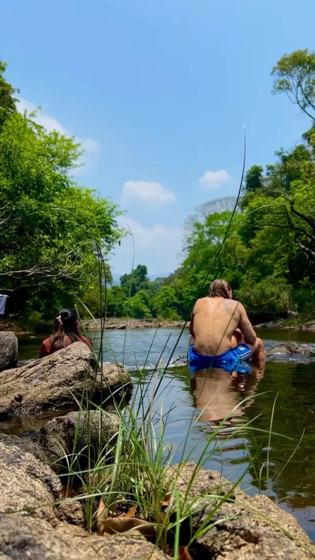 A guest relaxes in a shallow river pool shaded by trees