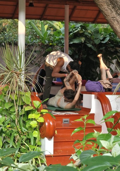 Yoga teacher assisting student in a yoga retreat Kerala session outdoors